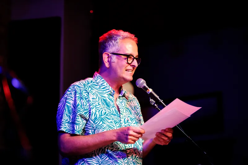 A combatant in a leaf-print shirt reading from pages at the microphone