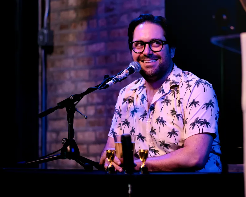 The timekeeper in a palm-tree shirt smiling into the microphone, trophies on the table