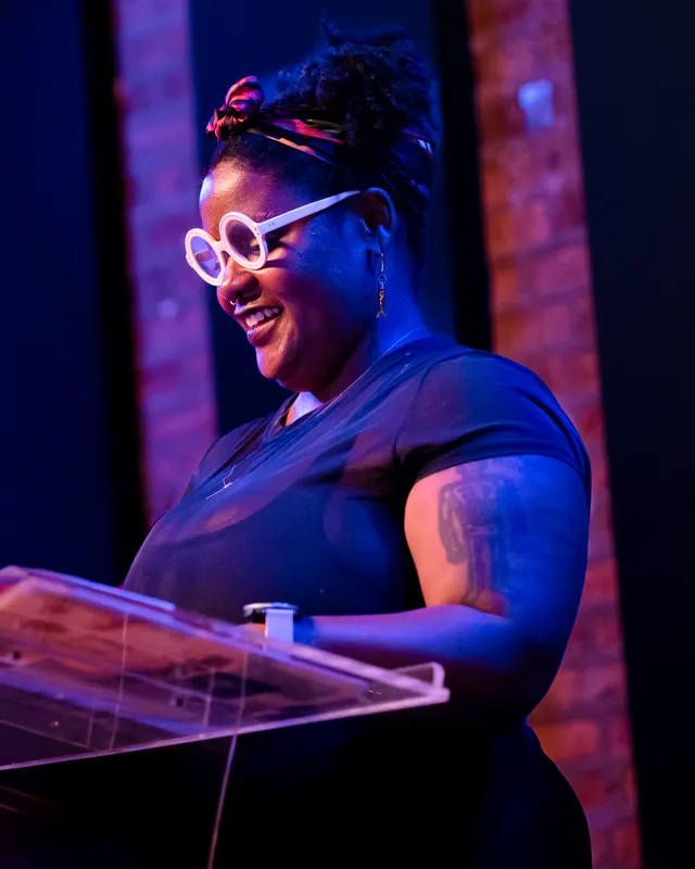 A combatant in round white glasses laughing at the lectern
